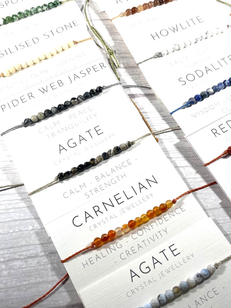Op de afbeelding: Assortiment van kleurrijke kralenarmbanden met verschillende edelsteensoorten en namen, waaronder spinnenwebjaspis, agaat, carneol, howliet, sodaliet en rode agaat. Elke armband heeft een bijbehorende beschrijving van de eigenschappen en voordelen van de steen.