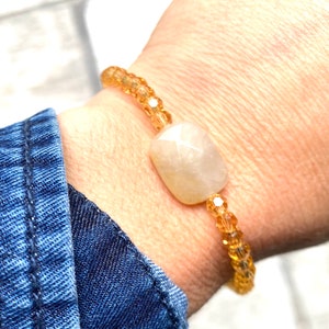 May include: A bracelet made with small, clear, amber-coloured beads and a larger, oval-shaped, white gemstone.