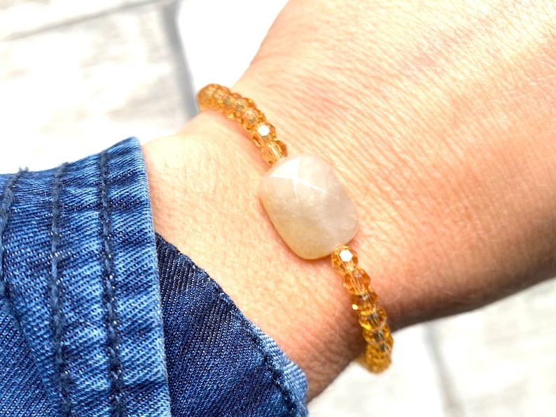 May include: A bracelet made with small, clear, amber-coloured beads and a larger, oval-shaped, white gemstone.