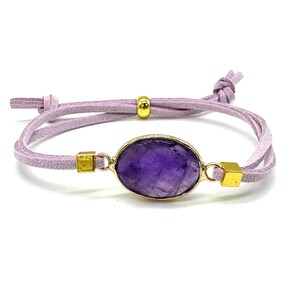 May include: A purple amethyst gemstone bracelet with gold accents and a light purple suede cord.