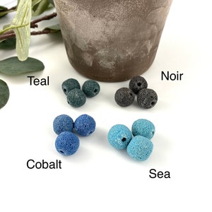 May include: Four sets of lava rock beads in different colors: teal, cobalt, sea, and noir. The beads are arranged in groups of three on a white surface.
