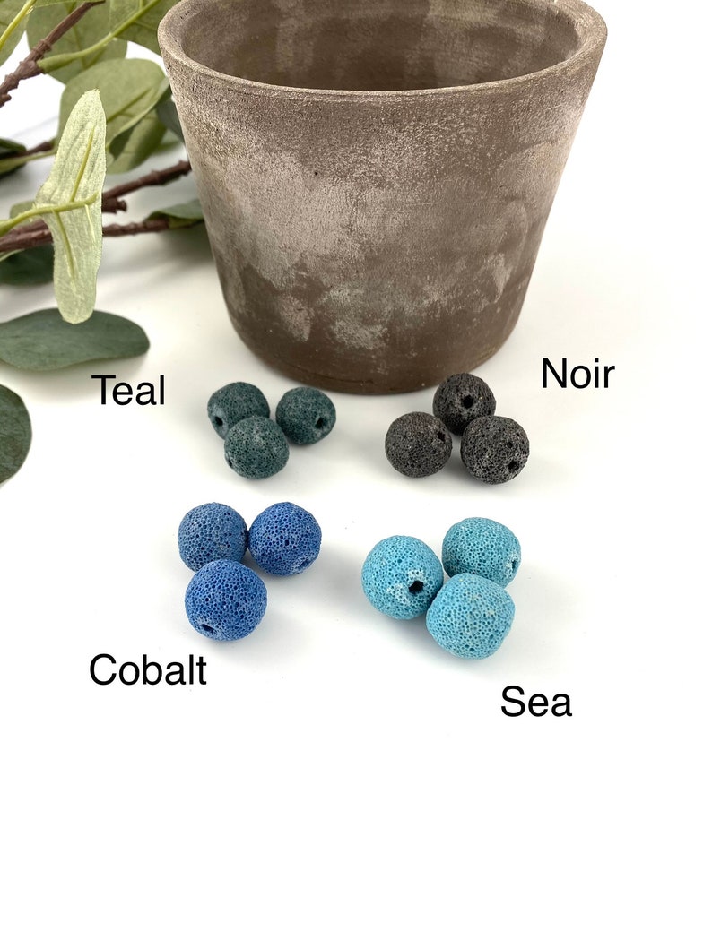 May include: Four sets of lava rock beads in different colors: teal, cobalt, sea, and noir. The beads are arranged in groups of three on a white surface.
