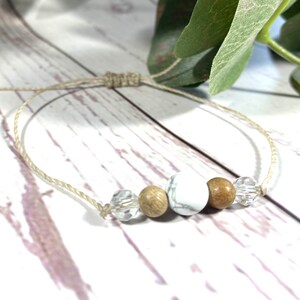 Puede incluir: Un brazalete sencillo hecho con materiales naturales. Tiene cuentas blancas y marrones, cuentas de cristal transparentes y un cord&oacute;n beige anudado.