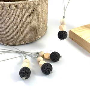 May include: Four gray lava stone and wood bead necklaces with gray cords. The necklaces are on a white surface.