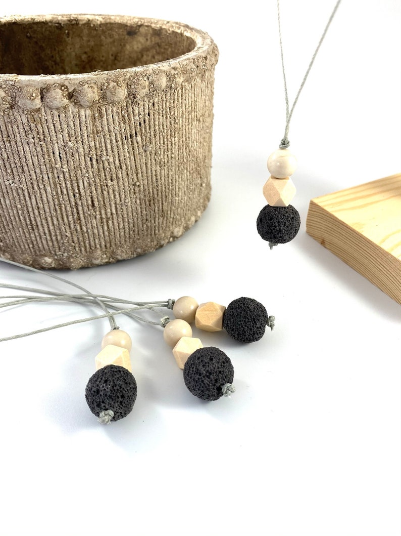 May include: Four gray lava stone and wood bead necklaces with gray cords. The necklaces are on a white surface.