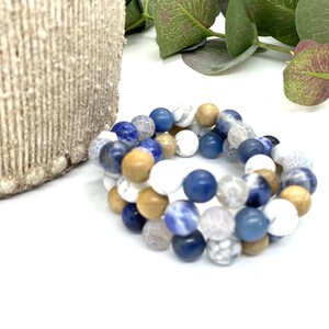 Puede incluir: Un brazalete de múltiples hilos hecho con cuentas azules, blancas y marrones. El brazalete está hecho con piedras naturales y madera.