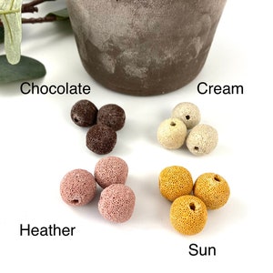 May include: Four sets of colorful lava rock beads in the colors chocolate, cream, heather, and sun. Each set contains three beads.