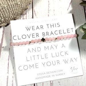 Puede incluir: Un brazalete de trébol rosa y dorado con el texto "Usa este brazalete de trébol y que la suerte te acompañe" y el texto "STOSA-DESIGN.COM HECHO A MANO EN SURREY".