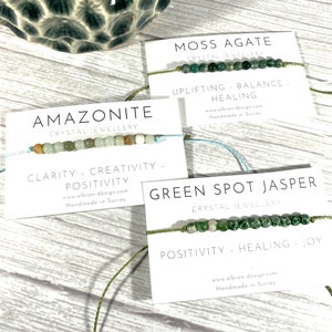 Op de afbeelding: Drie armbanden gemaakt van natuurlijke stenen en touw. De armbanden zijn gelabeld met het type steen en de bijbehorende helende eigenschappen. De stenen zijn Amazoniet, Mossaгат en Groene Vlekjaspis.