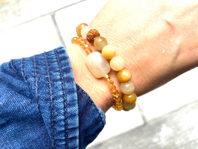 Pu&ograve; includere: Due braccialetti su un polso. Il braccialetto superiore &egrave; fatto di perline marroni chiare e beige con una perlina marrone scuro al centro. Il braccialetto inferiore &egrave; fatto di perline trasparenti e ambrate.