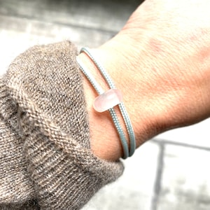Peut inclure: Un bracelet en cordon bleu clair avec une perle en verre de mer rose.