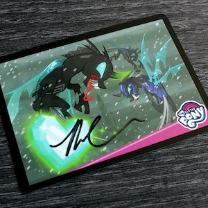 May include: A black and blue dragon card with a green heart and a signature. The card has a pink border and the text "My Little Pony" in white.