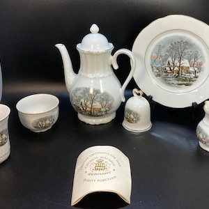 May include: A white porcelain tea set featuring a winter landscape scene with a house and trees. The set includes a teapot, a plate, a creamer, a cup, a bowl, and a bell. A paper tag reads: Made exclusively for Avon, Crown Bavaria, Germany, Quality Porcelain.