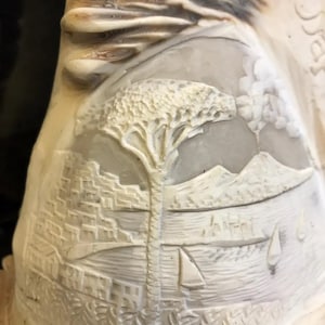 Pode incluir: Uma escultura de cerâmica branca que representa uma paisagem marítima com uma árvore no centro. A escultura é esculpida com detalhes de uma cidade, uma massa de água e veleiros.