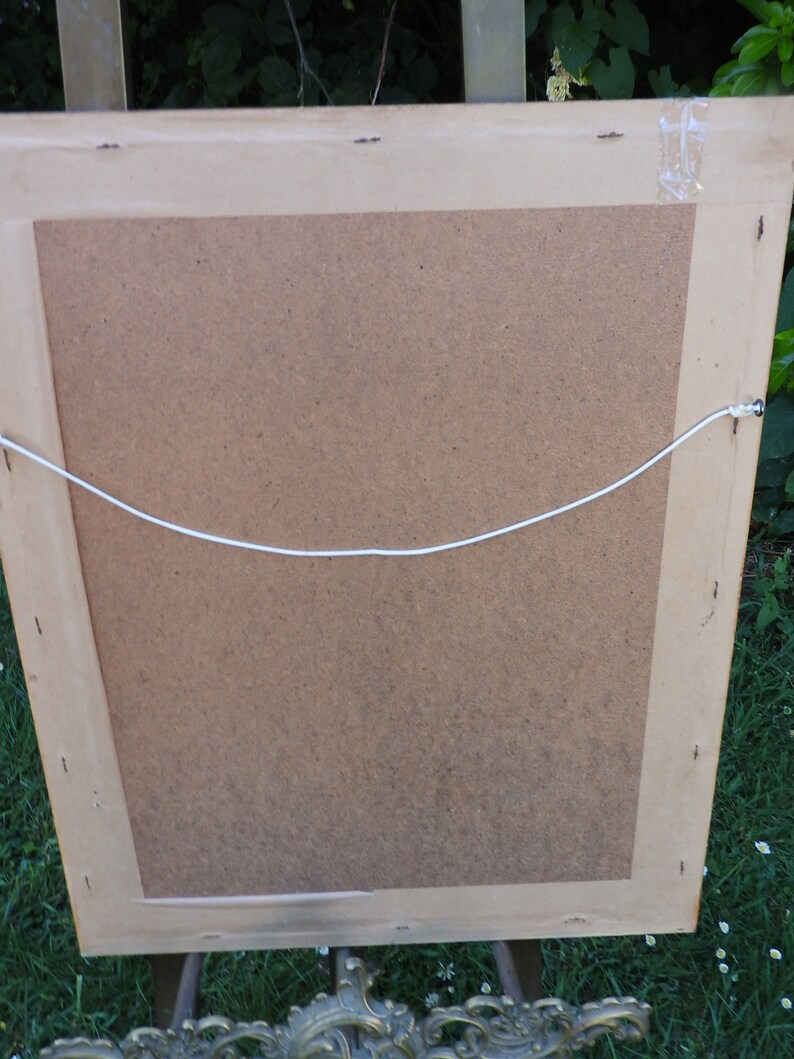May include: The back of a framed picture with a brown cardboard backing and a white string attached to the top for hanging.