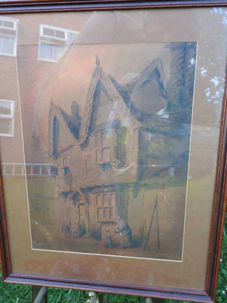 May include: A framed watercolor painting of a house with a gabled roof and a chimney. The house is painted in shades of brown and gray, and the background is a soft, muted green.