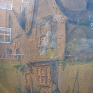May include: A watercolor painting of a brown cottage with a thatched roof. The cottage has two windows and a door. The painting is framed and has a light brown background.