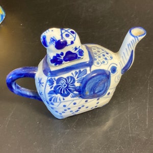 Könnte beinhalten: Eine blaue und weiße Keramik-Teekanne in Form eines Elefanten. Die Teekanne hat einen kleinen Elefanten auf dem Deckel. Die Teekanne ist mit blauen Blumendesigns verziert.