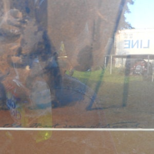 May include: A framed abstract painting with a blue and brown color scheme. The painting is titled "Art Jean with Moon" and is set against a blurry background of a building with the text "TAR LINE" on it.