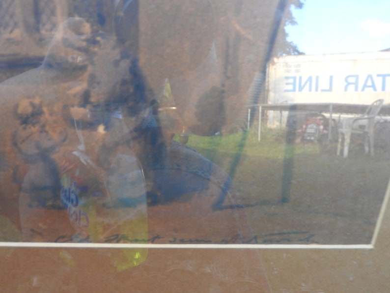 May include: A framed abstract painting with a blue and brown color scheme. The painting is titled "Art Jean with Moon" and is set against a blurry background of a building with the text "TAR LINE" on it.