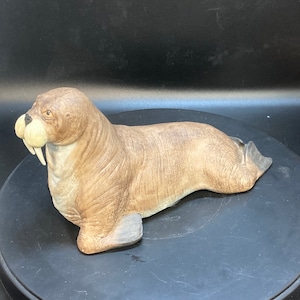 Könnte beinhalten: Eine braune und weiße Keramik-Walross-Figur mit detaillierter, strukturierter Oberfläche. Das Walross liegt auf dem Bauch und hat den Kopf zur Seite gedreht.