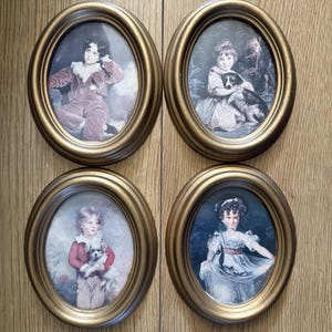 Può includere: Quattro ritratti ovali vintage incorniciati. Ogni cornice è color oro. I ritratti raffigurano bambini, alcuni con animali domestici, in abiti classici. I ritratti sono ambientati su uno sfondo di legno.