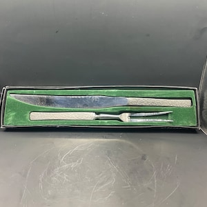 May include: A silver knife and fork set in a green velvet box. The knife has a textured handle and the fork has a three-pronged design.