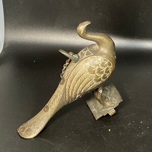 May include: A brass peacock figurine with intricate etched details. The peacock has a long tail and a raised head. The figurine is standing on a square base.