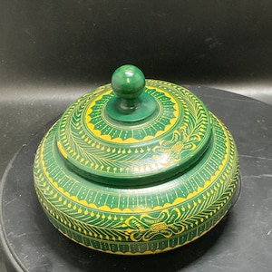 May include: A round, green wooden box with a lid. The box is decorated with yellow floral patterns.