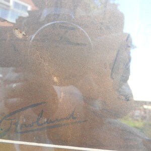 May include: A close-up of a framed artwork with a brown background and a black signature that reads "W.J.  Freund".