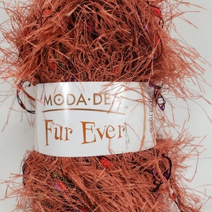 Pode incluir: Uma bola de fio cor de ferrugem com um rótulo que diz "Moda-De Fur Ever". O fio tem uma textura felpuda e é feito de uma mistura de fibras.