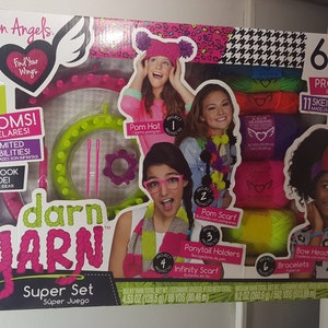 Può includere: Una scatola Fashion Angels Darn Yarn Super Set con immagini di ragazze che indossano progetti di filato. La scatola include 3 telai, 11 matasse di filato e istruzioni per realizzare un cappello con pompon, una sciarpa, fermacoda, sciarpa infinity, fascia per capelli e braccialetti.
