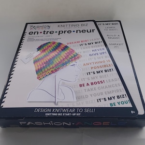 May include: A Fashion Angels Knitting Biz Start-Up Kit. The box features a colorful knitted hat design and the text "Design Knitwear to Sell!" and "It's My Biz!" The kit is for ages 8+.