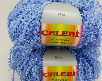 May include: Two balls of light blue yarn with a fluffy texture. The yarn is labelled "Celebi Purpur" and "50 gr."