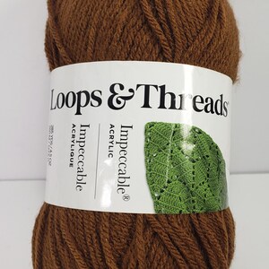 May include: A skein of solid brown acrylic yarn with a white paper label. The label features the text Loops & Threads Impeccable, a graphic of a green crocheted leaf, and the weight specification of 4.5 oz and 285 yards for this craft supply.