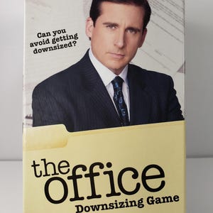 May include: The Office Downsizing Game box features a photo of Steve Carell. The box has the text "Can you avoid getting downsized?" and "The Office Downsizing Game". The game is for ages 16+ and requires knowledge of English.