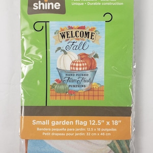 Peut inclure: Un petit drapeau de jardin de 32 cm sur 46 cm dans un emballage plastique. Le drapeau présente un fond bleu avec des citrouilles dans un seau en métal, le texte WELCOME Fall et Hand Picked Farm Fresh PUMPKINS. L'emballage indique rain or shine.