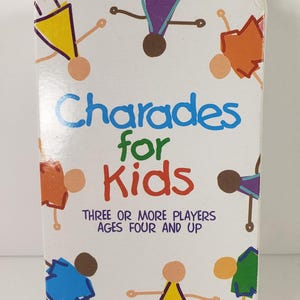 May include: A white box of "Charades for Kids" by Pressman. The box features colorful illustrations of stick figures and text that reads "Three or More Players Ages Four and Up". A choking hazard warning is also present.