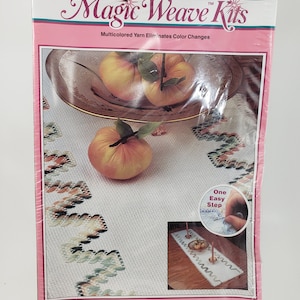 Könnte beinhalten: WonderArt Magic Weave Kits-Paket mit einem Country Sage Tischläufer-Bastelprojekt. Die Verpackung zeigt eine Nahaufnahme des fertigen Tischläufers mit einem dekorativen Rand und drei Äpfeln in einer Schale. Die Verpackung enthält auch Anweisungen für das Projekt, das als "Ein einfacher Schritt" beschrieben wird. Die Verpackung gibt an, dass das Projekt "Einfach an einem Wochenende zu machen ist" und ein Nettogewicht von 340 Gramm hat.