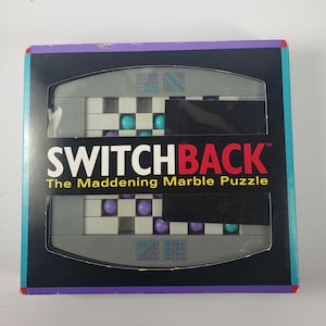 May include: A boxed Switchback marble puzzle. The box is black with teal and purple trim. The puzzle features a gray and white grid with teal and purple marbles. The text "SWITCHBACK The Maddening Marble Puzzle" is printed on the front.
