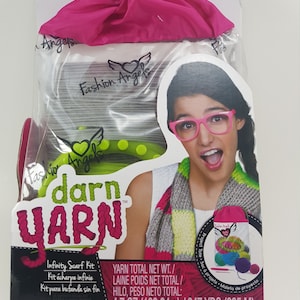 Può includere: Un kit di filato rosa e verde con una borsa a cordoncino rosa, una sciarpa grigia e bianca e una ragazza con occhiali rosa. Il kit include 4,7 once (133,24 grammi) di filato ed è sufficiente per realizzare una sciarpa infinita. Il kit si chiama "darn yarn" ed è realizzato da Fashion Angels.