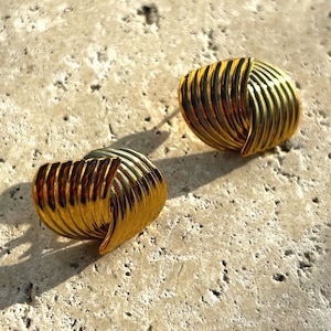 Könnte beinhalten: Ein Paar goldfarbene Ohrringe mit einem einzigartigen, geometrischen Design. Die Ohrringe bestehen aus mehreren überlappenden, geschwungenen Formen, die einen strukturierten, geschichteten Look erzeugen.