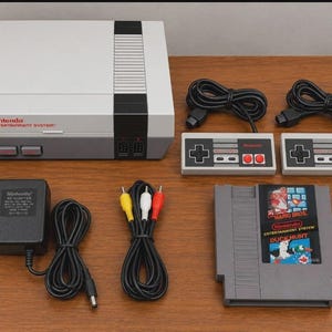 Puede incluir: Una consola Nintendo Entertainment System en gris y blanco, que incluye dos mandos rectangulares con botones negros, grises y rojos, un adaptador de corriente negro, un cable RCA con conectores amarillo, blanco y rojo, y un cartucho de juego Super Mario Bros./Duck Hunt.