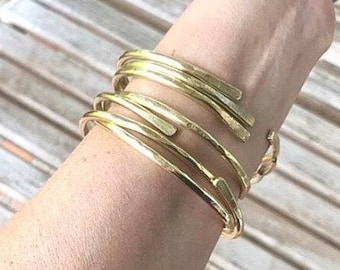 May include: A set of five gold-toned metal bangles stacked on a person's wrist. The bangles are all different widths and have a hammered texture.