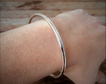 May include: A simple silver bangle bracelet, worn on a person's wrist.