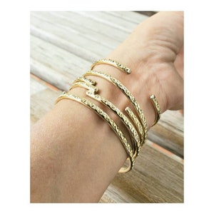 May include: A set of five gold-toned bangles with a textured diamond pattern. The bangles are stacked on a person's wrist.