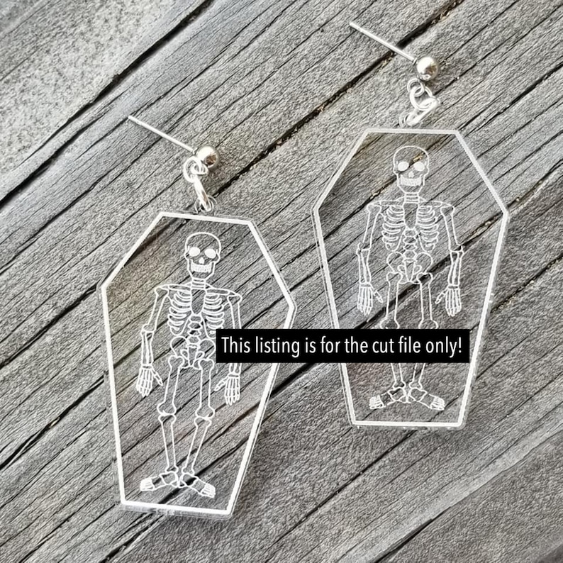 May include: A pair of clear acrylic earrings shaped like coffins with a skeleton inside each coffin.  The earrings are silver and have a small silver bead at the top.