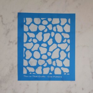 May include: Blue plastic stencil with a white cow print pattern. The stencil says "This or That Crafts - Cow Pattern" at the bottom.