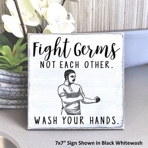 May include: A whitewash wood sign with black text that reads "Fight Germs Not Each Other. Wash Your Hands."  A black and white illustration of a person washing their hands is in the center of the sign. The sign is 7 inches by 7 inches.
