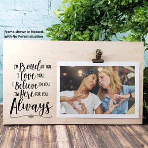 May include: A wooden photo frame with a clip at the top. The frame has a message that reads "I'm Proud of You. I Love You. I Believe in You. I'm Here for You. Always." A photo of two women is displayed in the frame.